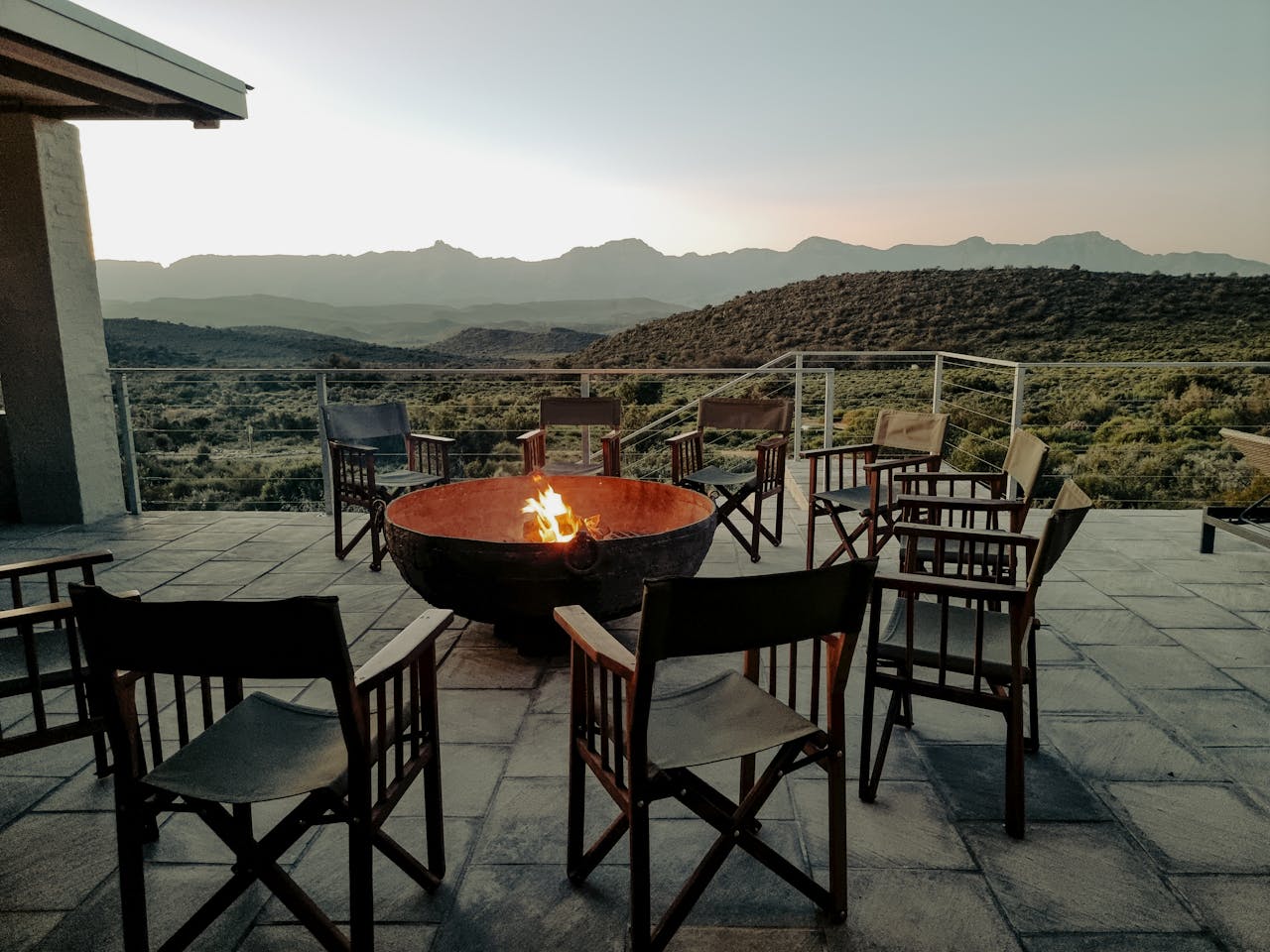 Scenic mountain view from a cozy balcony with a blazing fire pit surrounded by chairs.